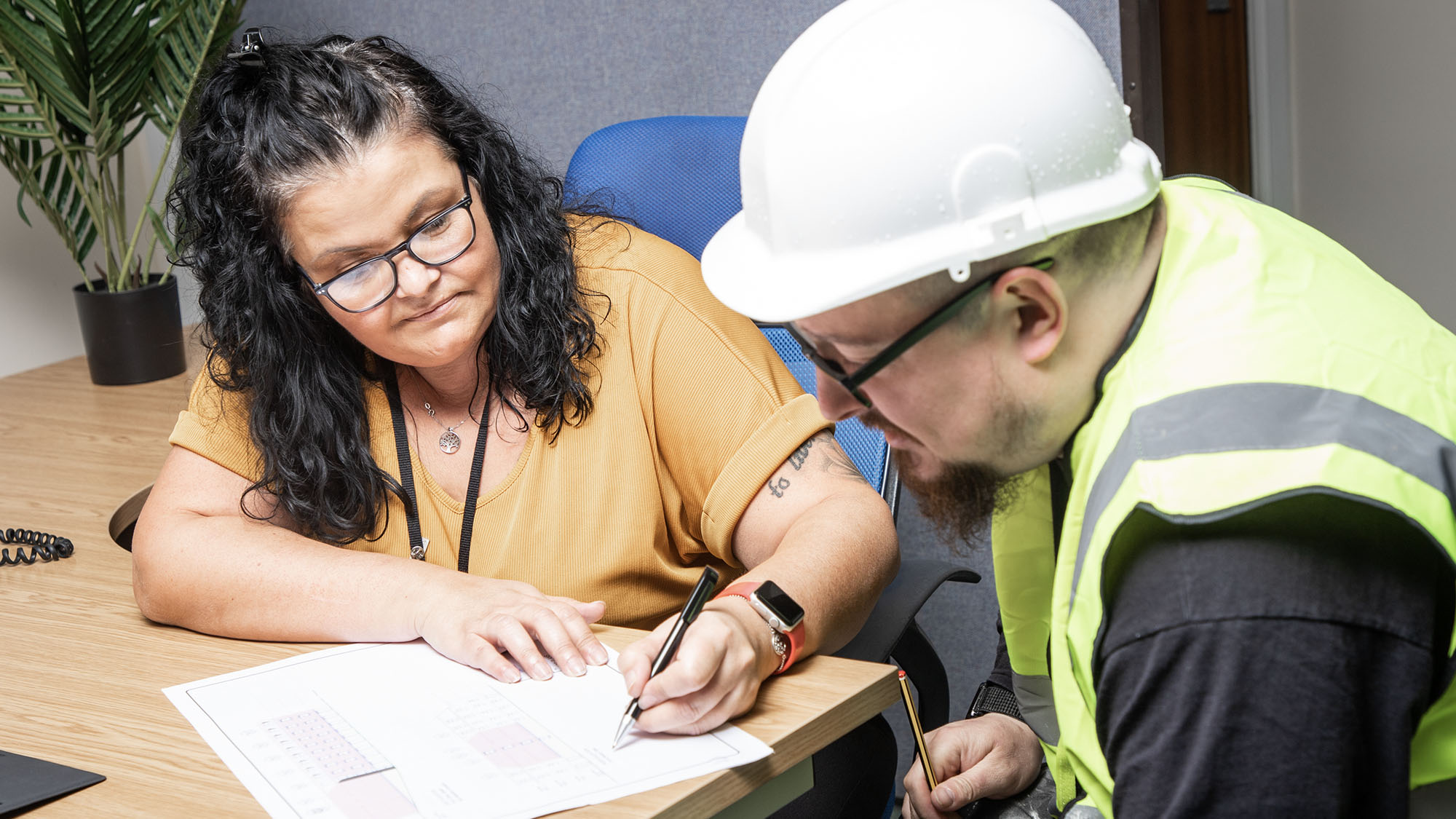 A Jiggle staff member is discussing a document with a candidate wearing a hard hat and high-visibility vest