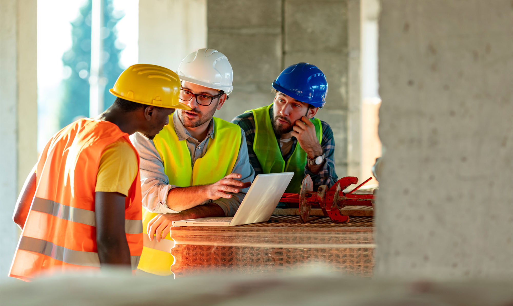 Three construction workers in conversation, working from a laptop.