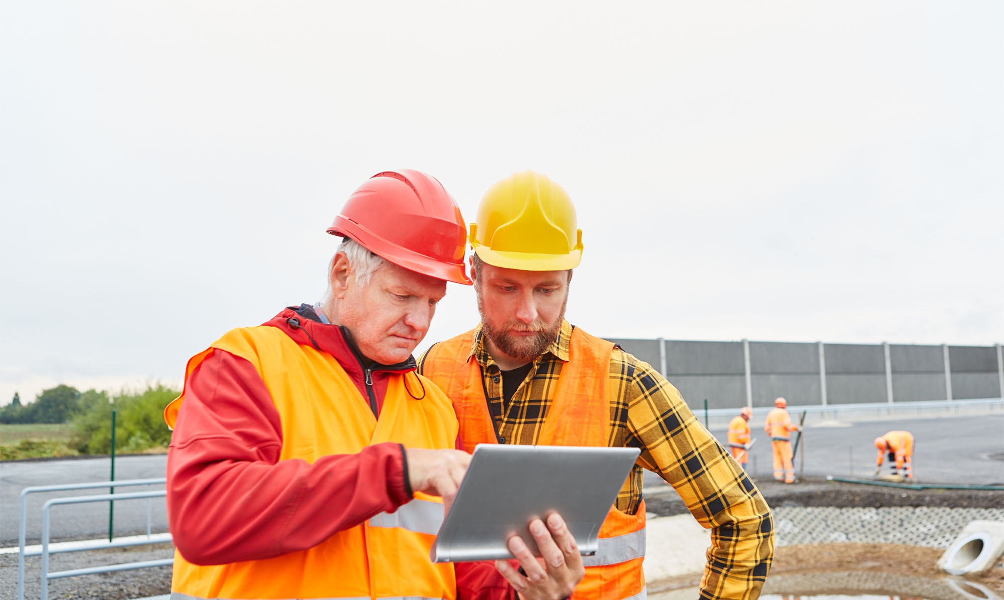 Construction workers in conversation, looking at tablet computer.