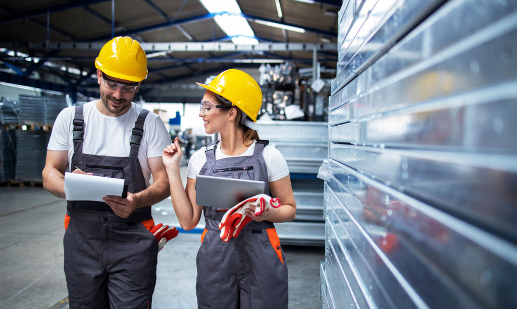 Two factory workers wearing safety gear in conversation.