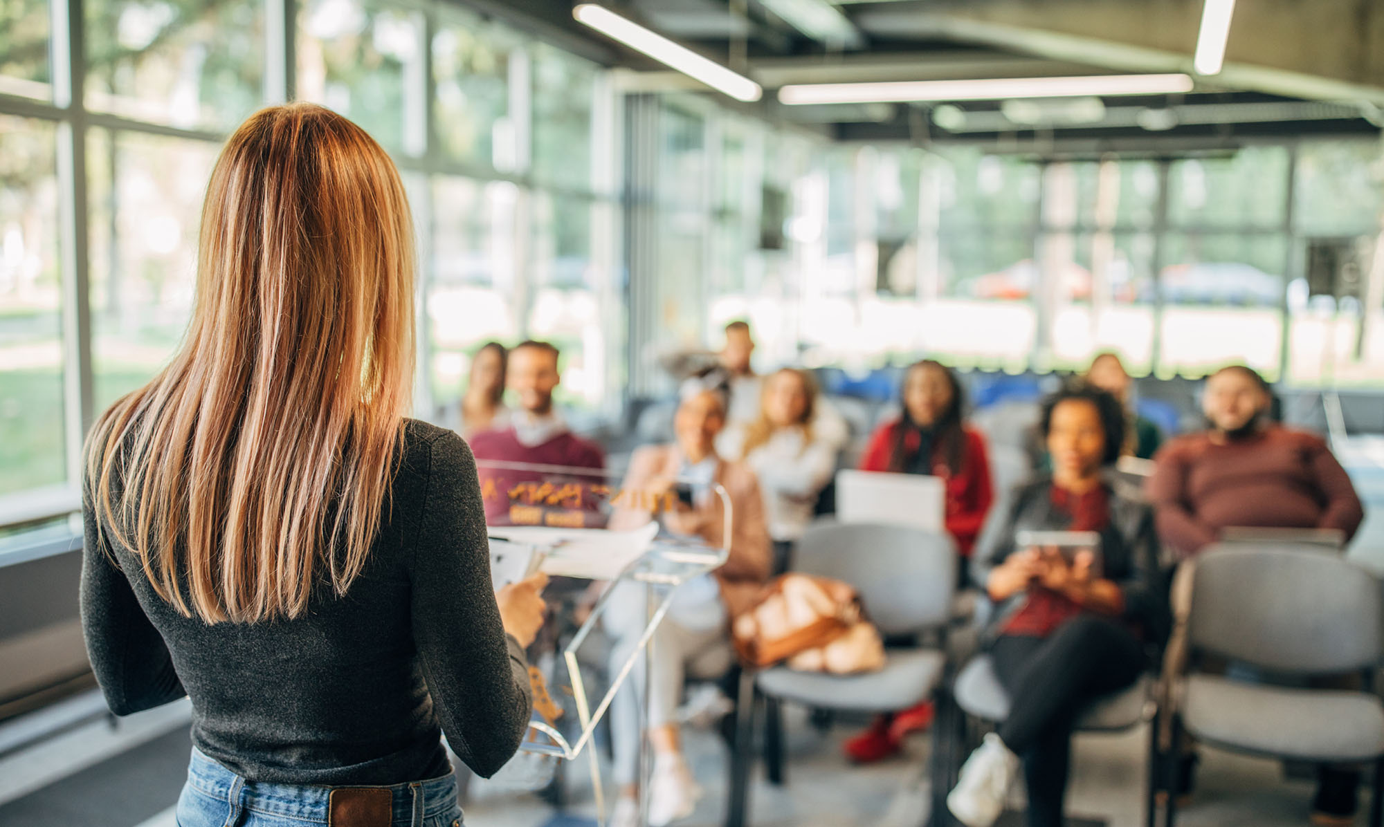 Woman stood up, addressing a room full of people.